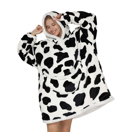 Person cozy in oversized blanket hoodie with cow pattern.