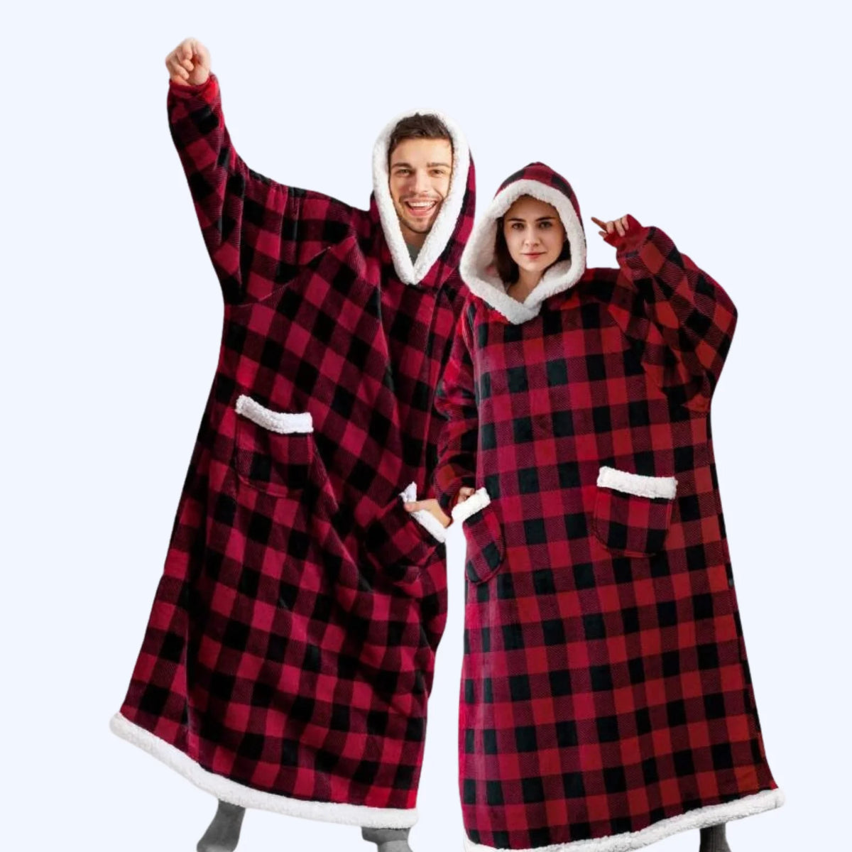 A man and a woman wearing matching black and red hoodie blankets with white faux-fur trim, standing against a light gray studio background.