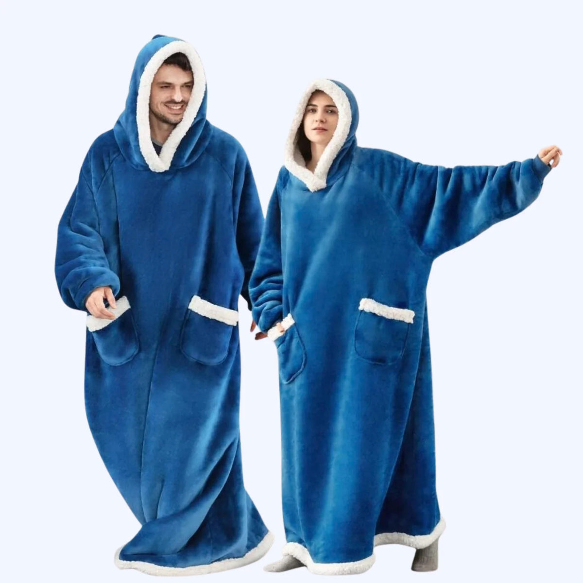 A man and a woman wearing matching blue hoodie blankets with white faux-fur trim, standing against a light gray studio background.