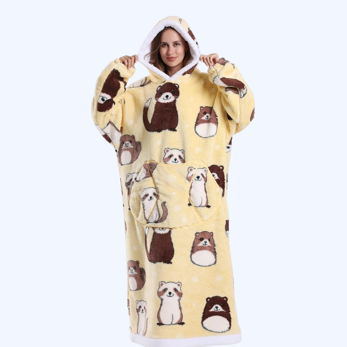 A woman wearing a hoodie blanket with a yellow background and an all-over otter print, holding up the hood against a light blue studio background
