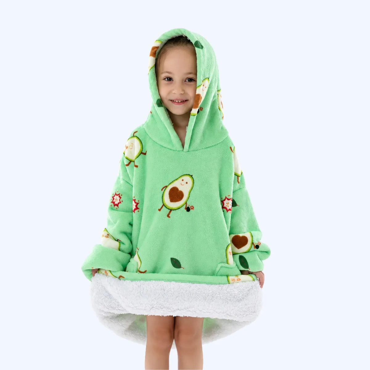 A young child wearing a light green hoodie blanket with avocado and flower prints, standing against a plain light gray background.