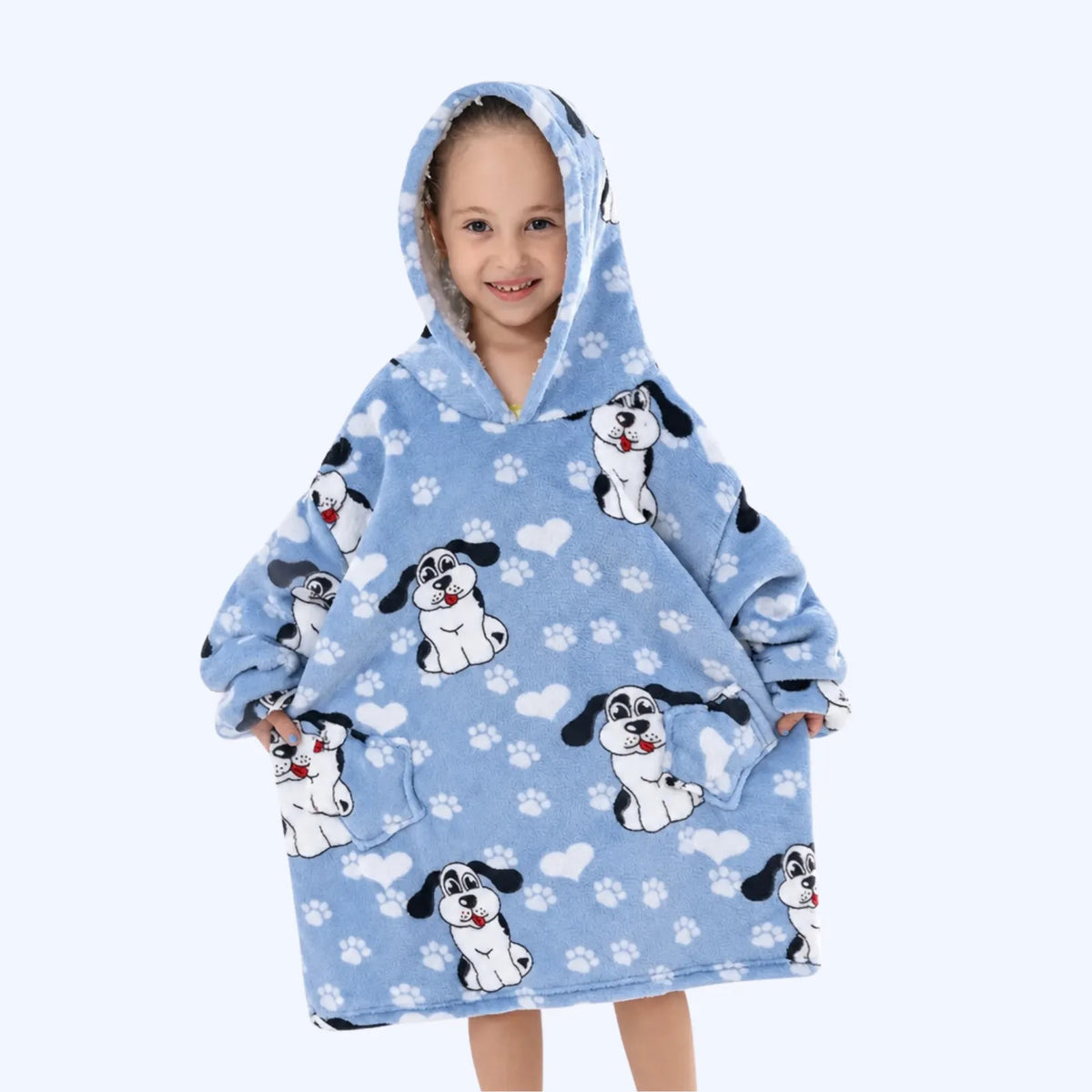 A young child wearing a light blue hoodie blanket with a cartoon dog print and white paw prints, standing against a plain light gray background.