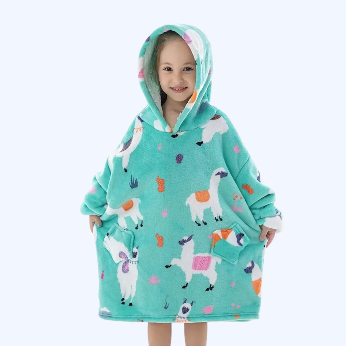 A young child wearing a hoodie blanket with a colorful llama print, standing against a plain light gray background.