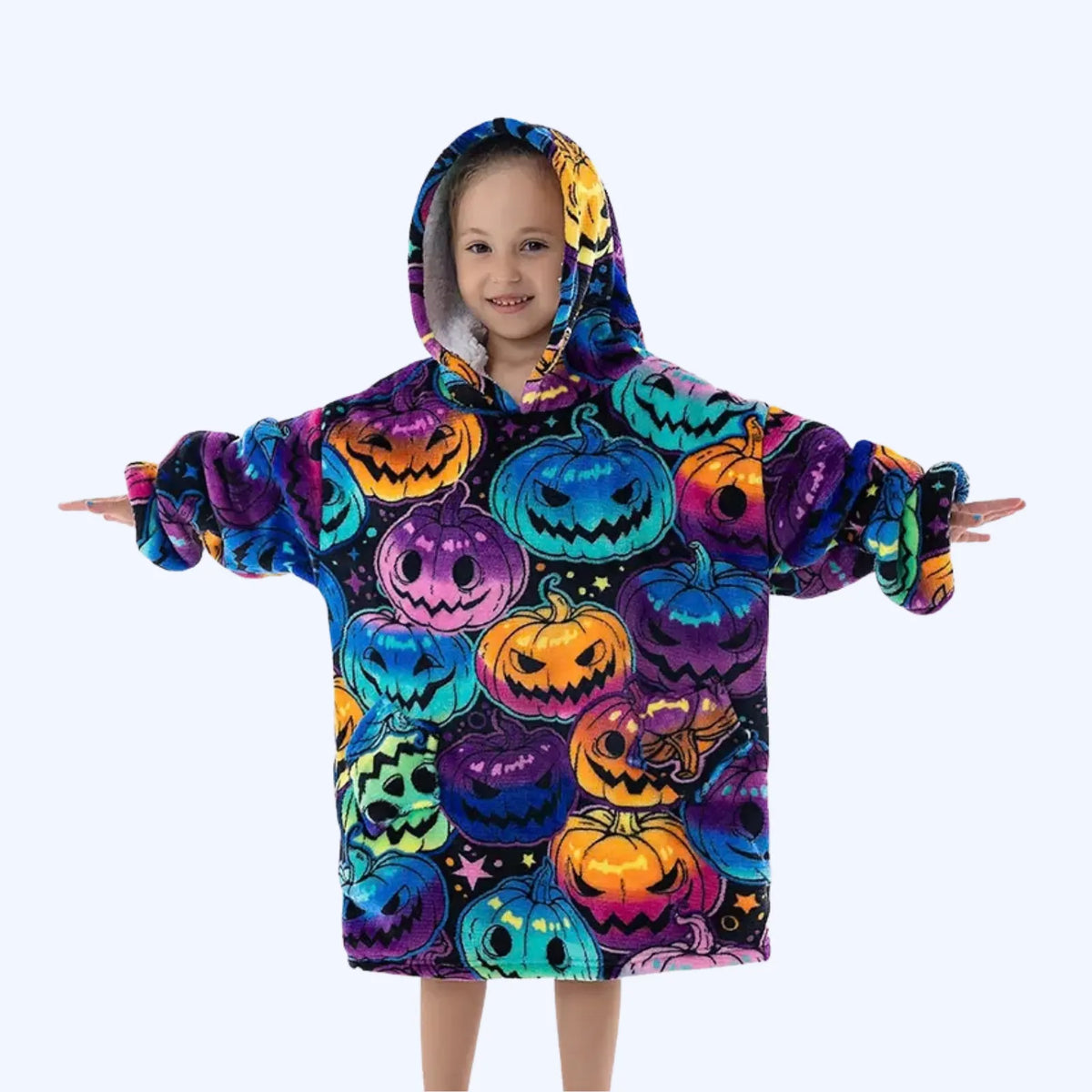 A child wearing a hoodie blanket covered in a colorful Halloween pumpkin print, standing against a light gray background with arms outstretched.