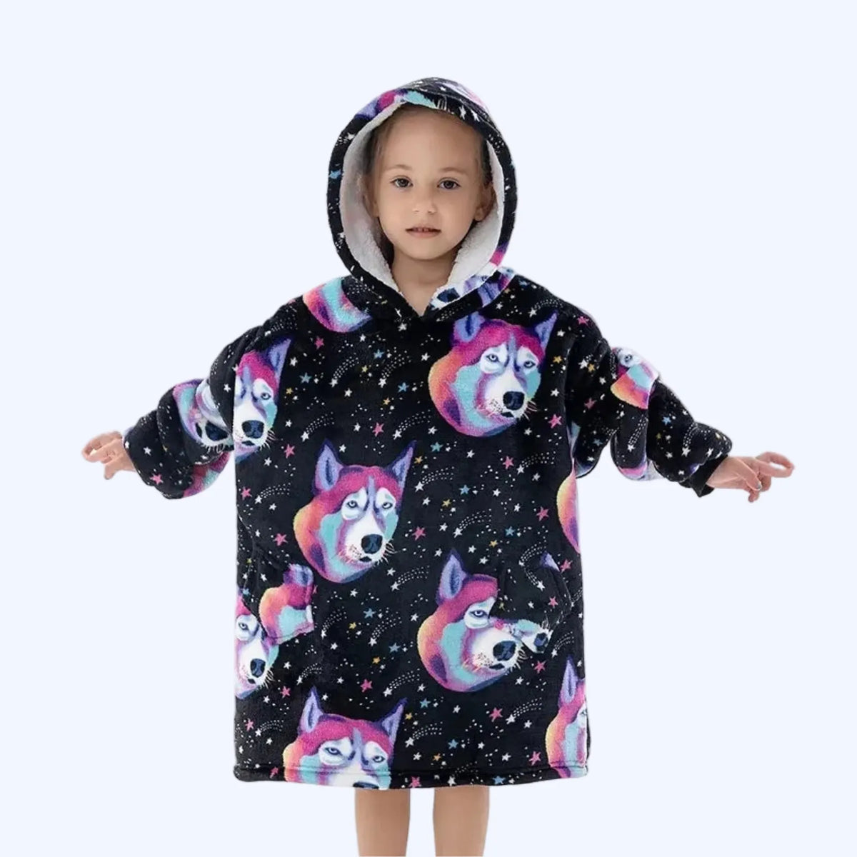 A young child wearing a hoodie blanket or poncho with a black space print featuring colorful husky dog faces and stars.