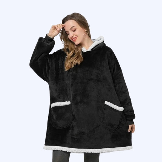 A woman wearing a black hoodie blanket with white sherpa lining and two pockets. 