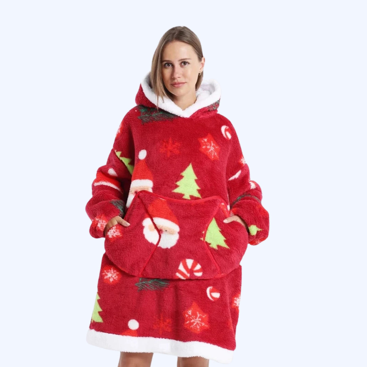 A woman wearing a red hoodie blanket with a white faux-fur trim and a festive Christmas print featuring Santa Claus, Christmas trees, snowflakes, and candy canes.