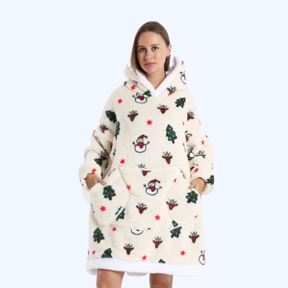 A woman wearing a cream-colored hoodie blanket with a festive Christmas print of Santa Claus, reindeer, and Christmas trees.
