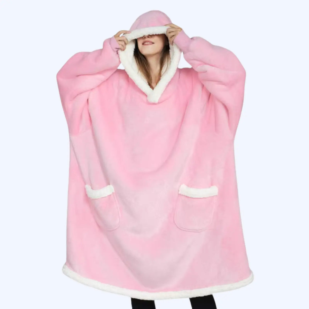 A woman wearing a pink hoodie blanket with white sherpa lining and two pockets. 